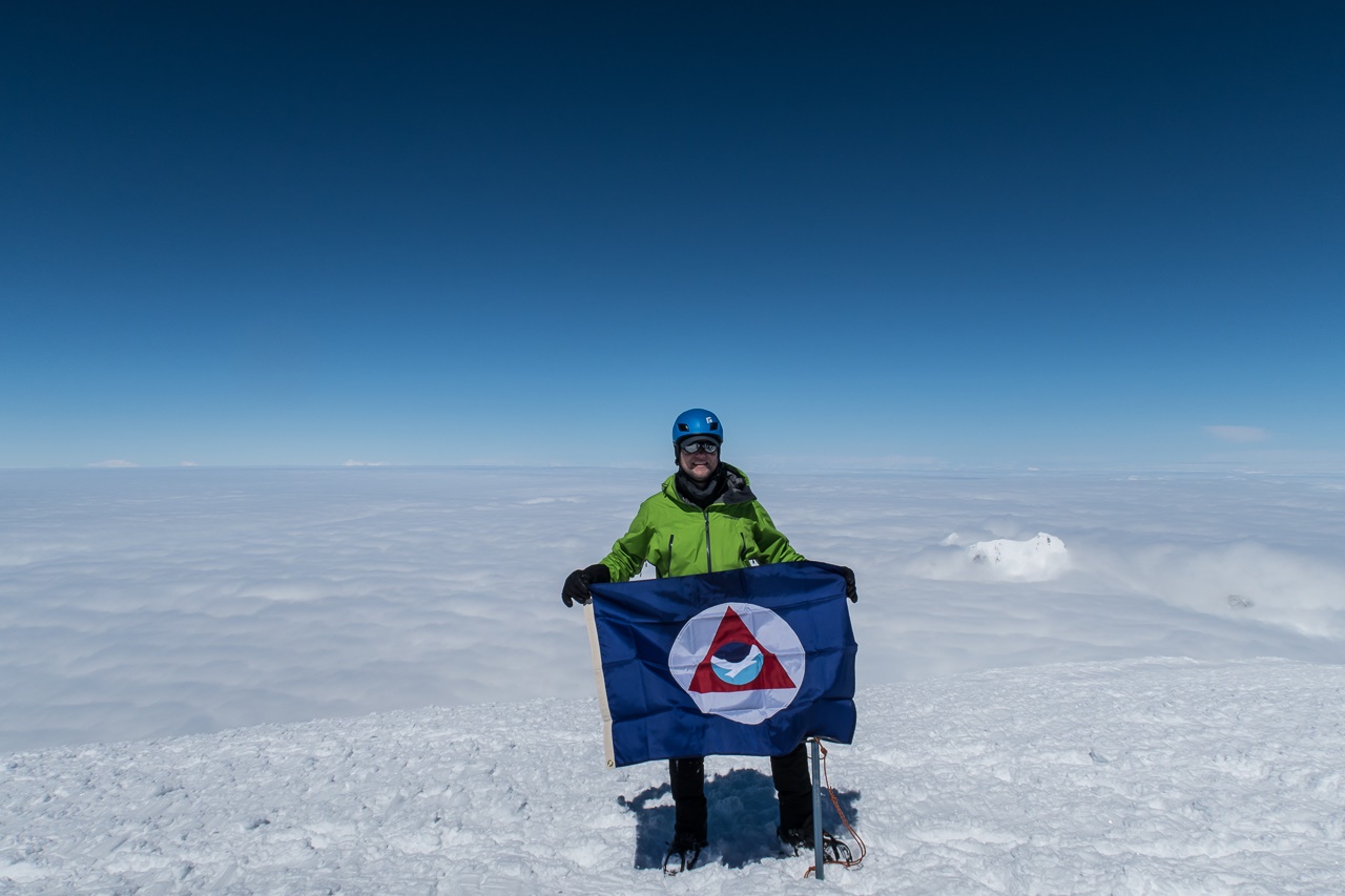 Cmdr. Van Waes holds the NOAA flag atop the summit of Mount Fairweather.
